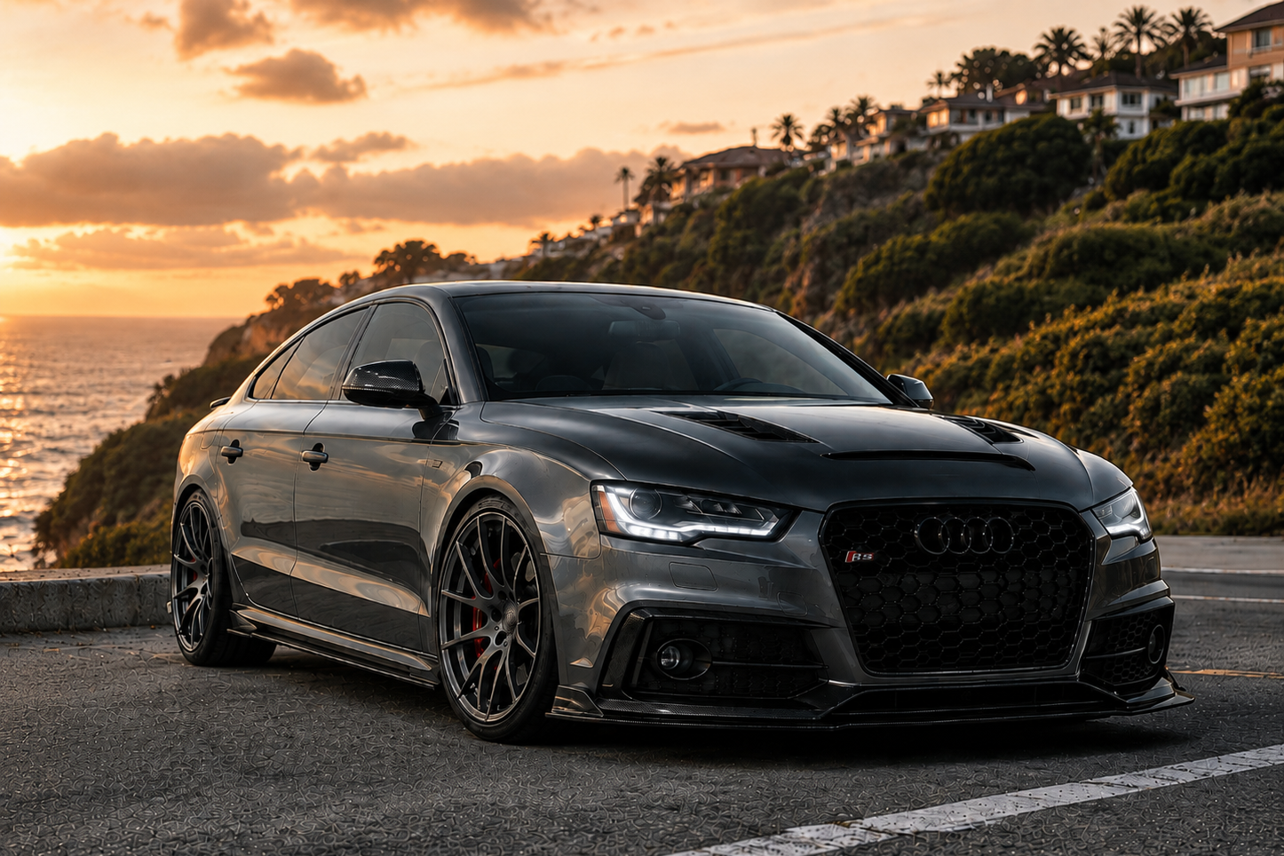 Modified Audi sedan with carbon fiber styling accents, collection banner for Audi exterior parts, positioned along a costal road-side